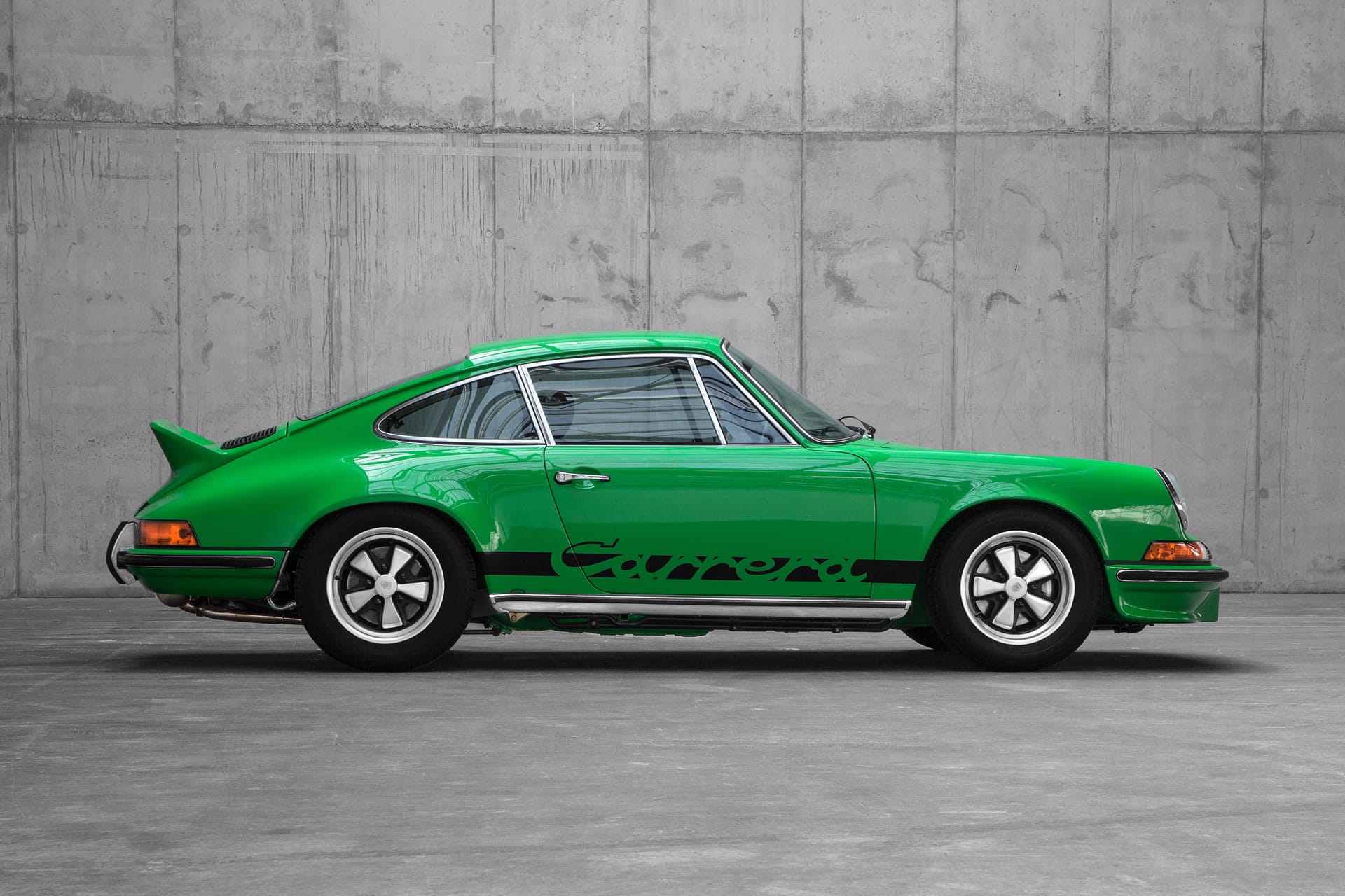 Viperngrüner Porsche Carrera RS 2.7 von 1973 im Seitenprofil vor einer Betonwand
