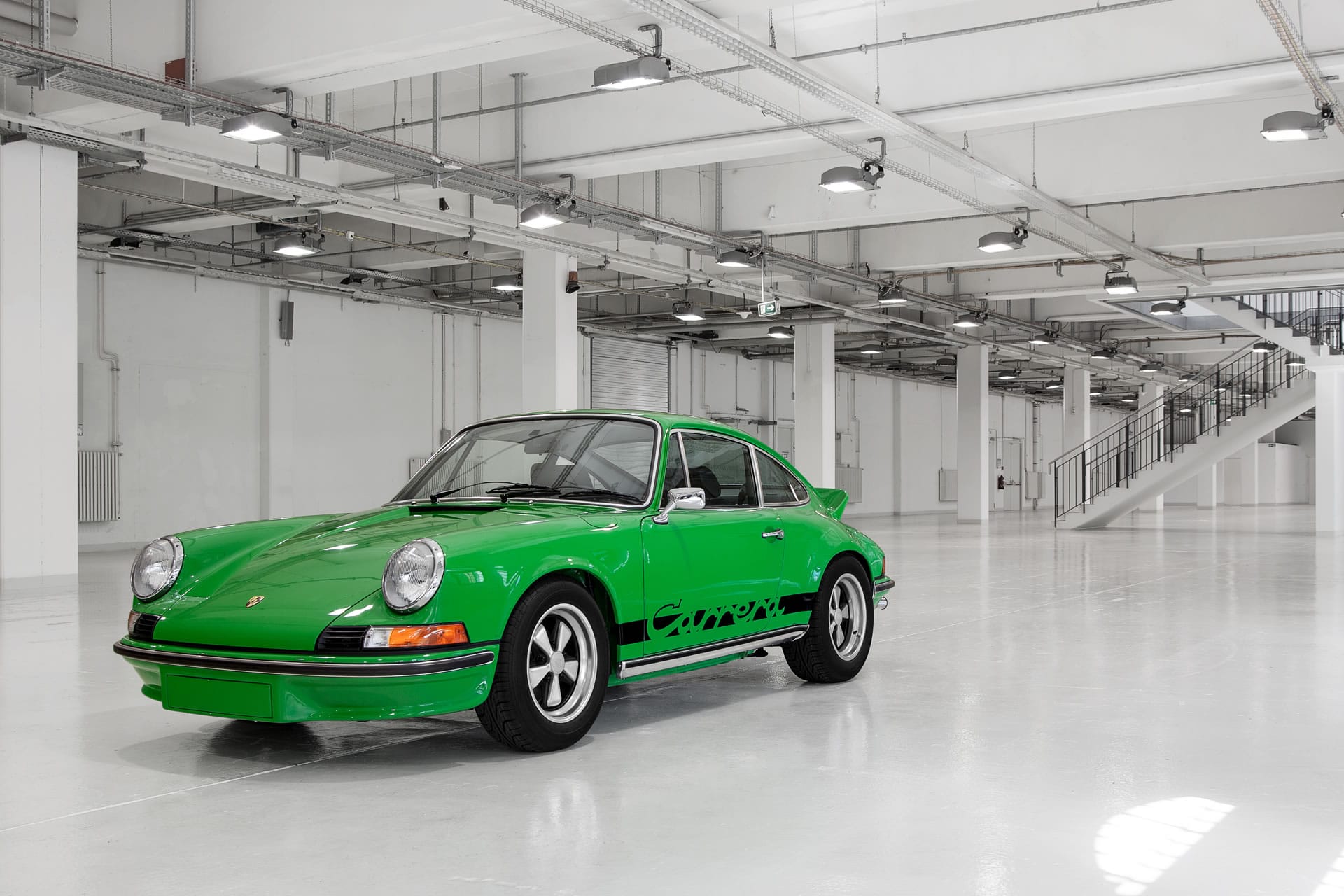 Viperngrüner Carrera RS 2.7 in der Halbfront in einer hellen Halle, mit Fuchs-Felgen und dem Carrera-Schriftzug auf der Flanke